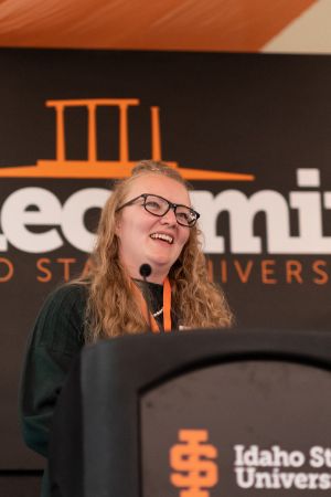 Jessica McBean stands at a podium that has ISU's logo on it, with a background banner that says