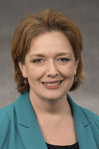 A woman with light skin and short red hair wearing a teal cardigan and black shirt, smiling.