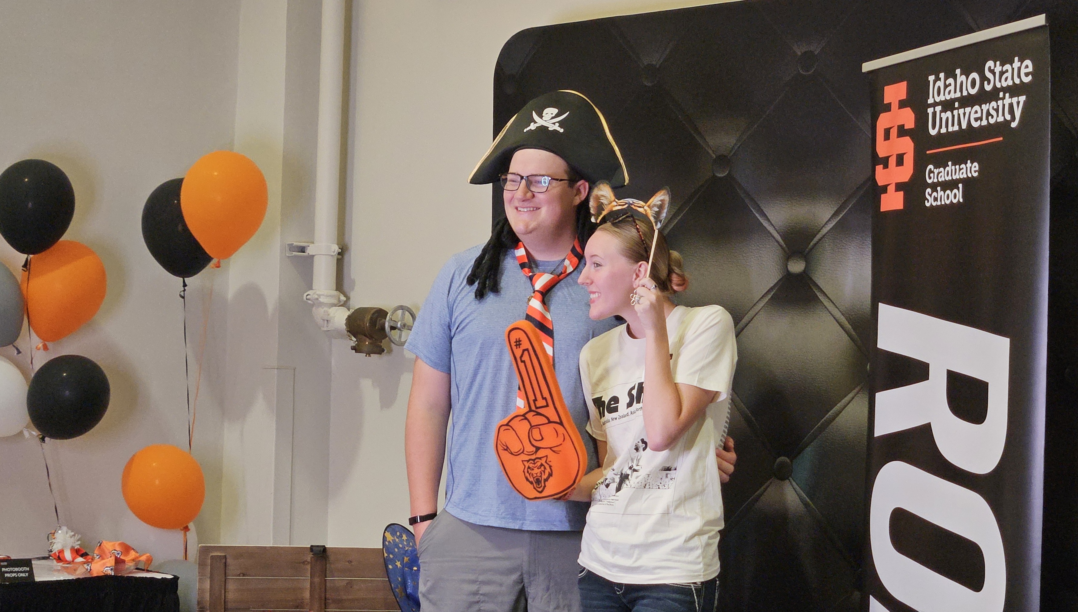 Two students posing with photobooth props while they get their picture taken in front of an ISU Graduate School backdrop