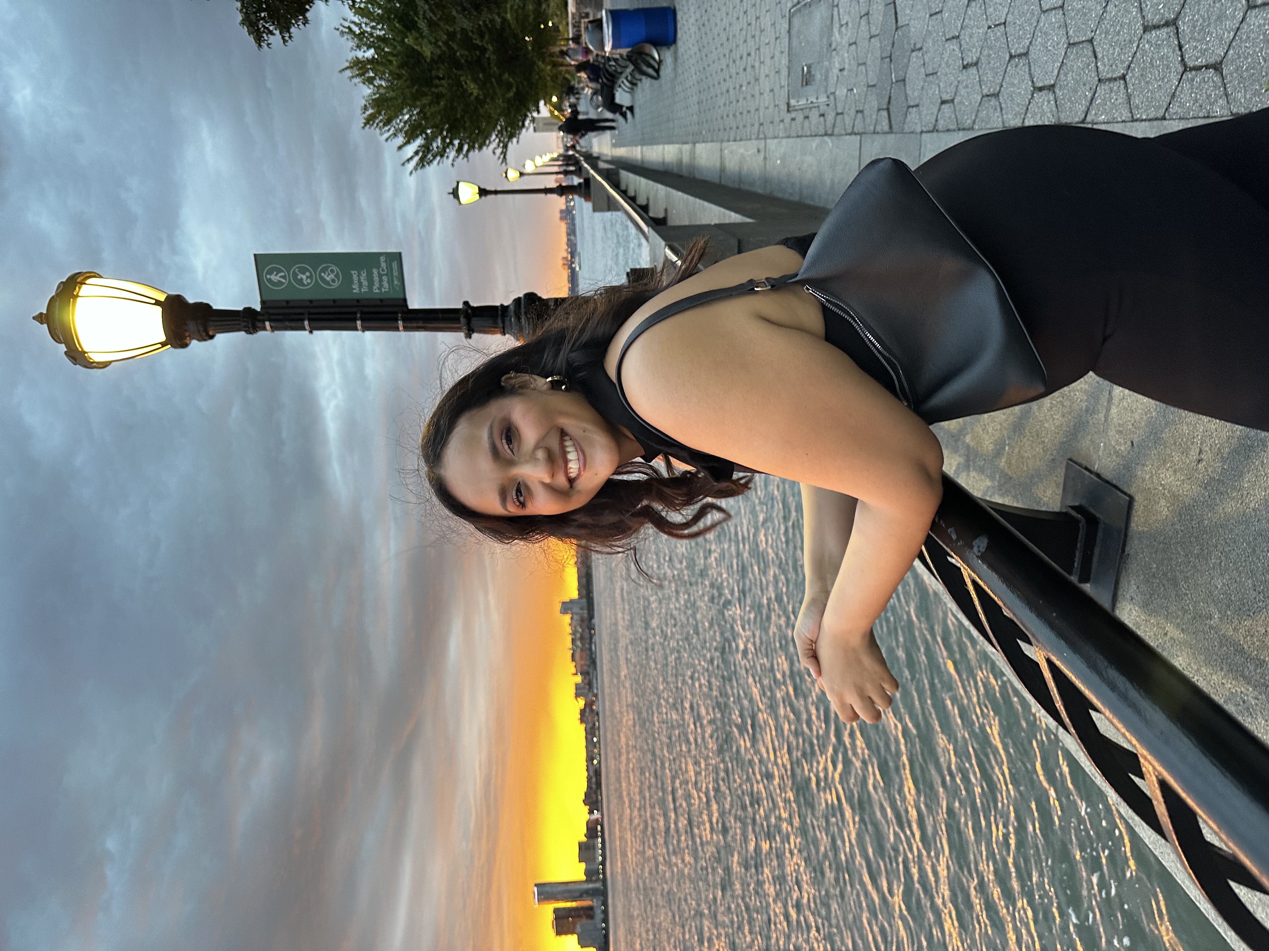 Woman stands in front of ocean and skyline with a black bag