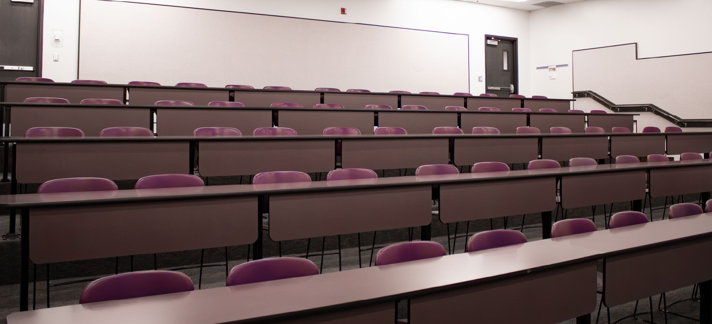 Tiered classroom at ISU Idaho Falls with fixed rows of long tables and purple chairs arranged in ascending levels.