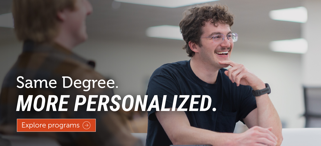 Student smiling while working with an advisor in a classroom setting. Text overlay reads “Same Degree. More Personalized.” with an “Explore programs” button.
