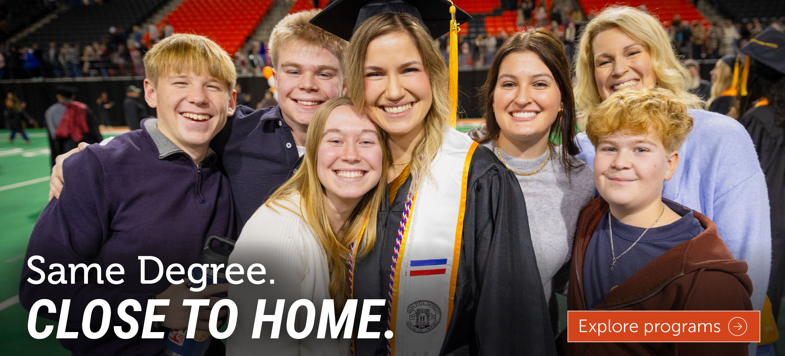 A smiling graduate in a cap and gown poses with family members during commencement. The image includes the text, 
