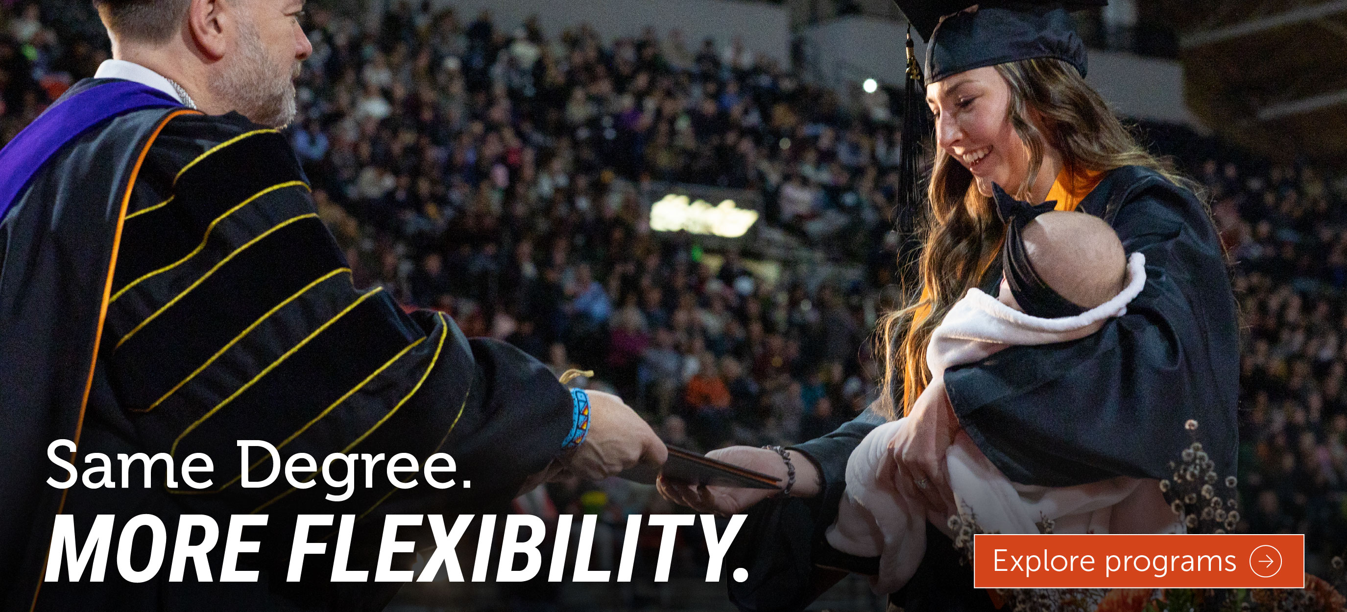 A graduate wearing a cap and gown accepts a diploma while holding a baby during a commencement ceremony. The image includes the text, 