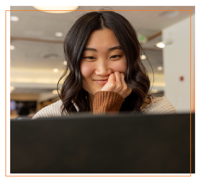Student smiling while using a laptop in a campus setting, representing registering for college classes online.