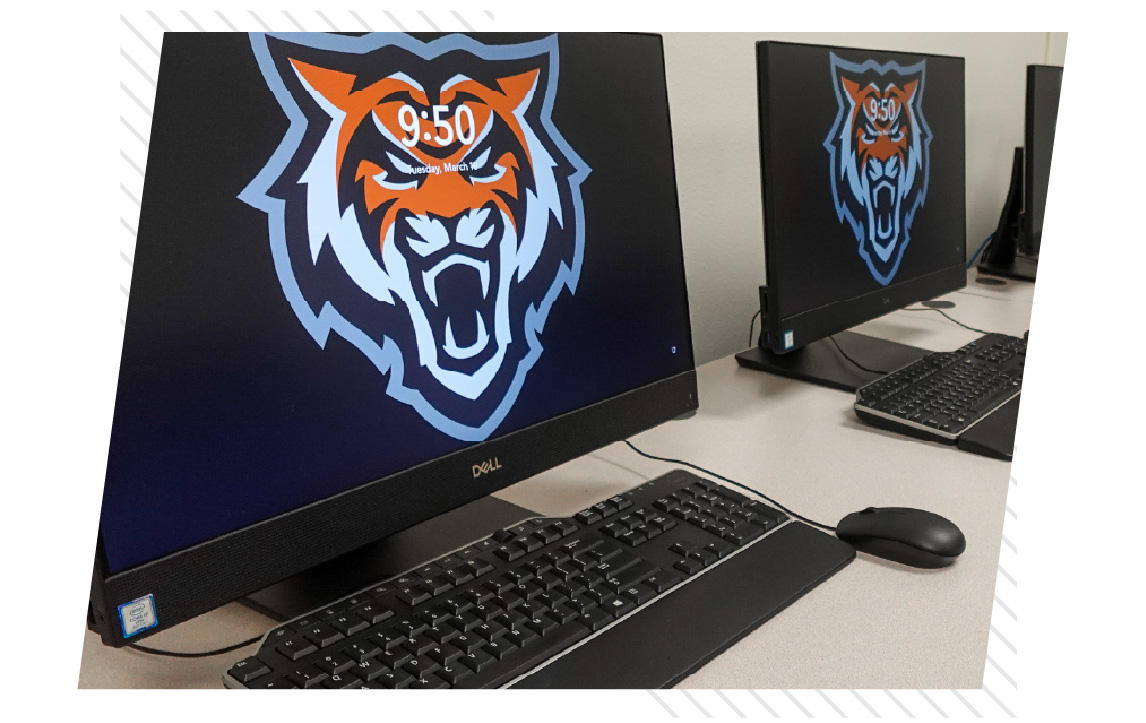 Close-up of desktop computers in a campus lab, with keyboards and mice on the desks and screens displaying the Idaho State Bengals logo.