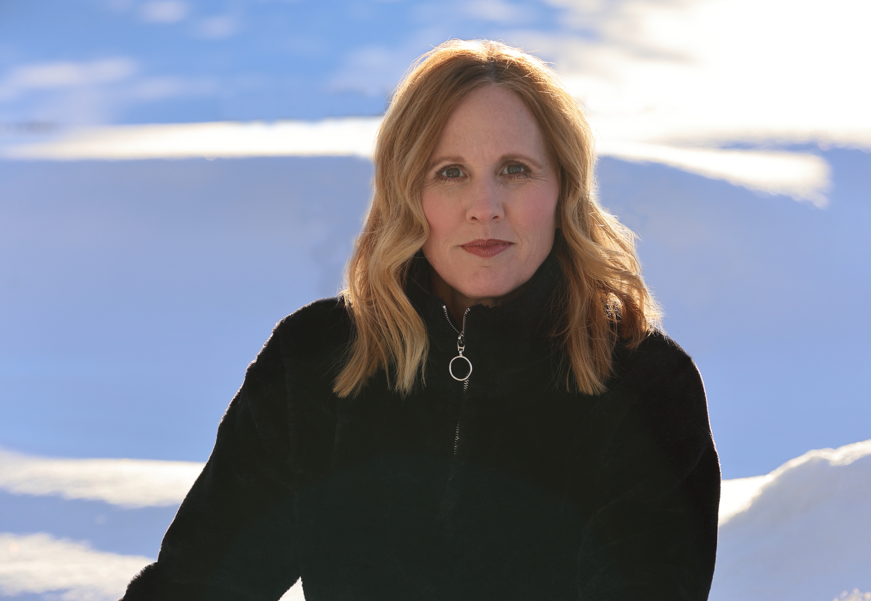 A women in a black coat with blue sky, Kris Millgate's headshot