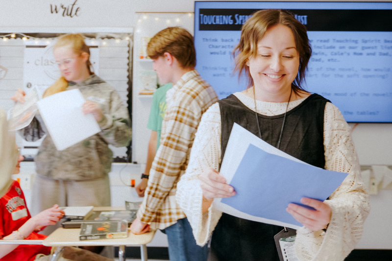 Teacher smiling at papers walking through a classroom