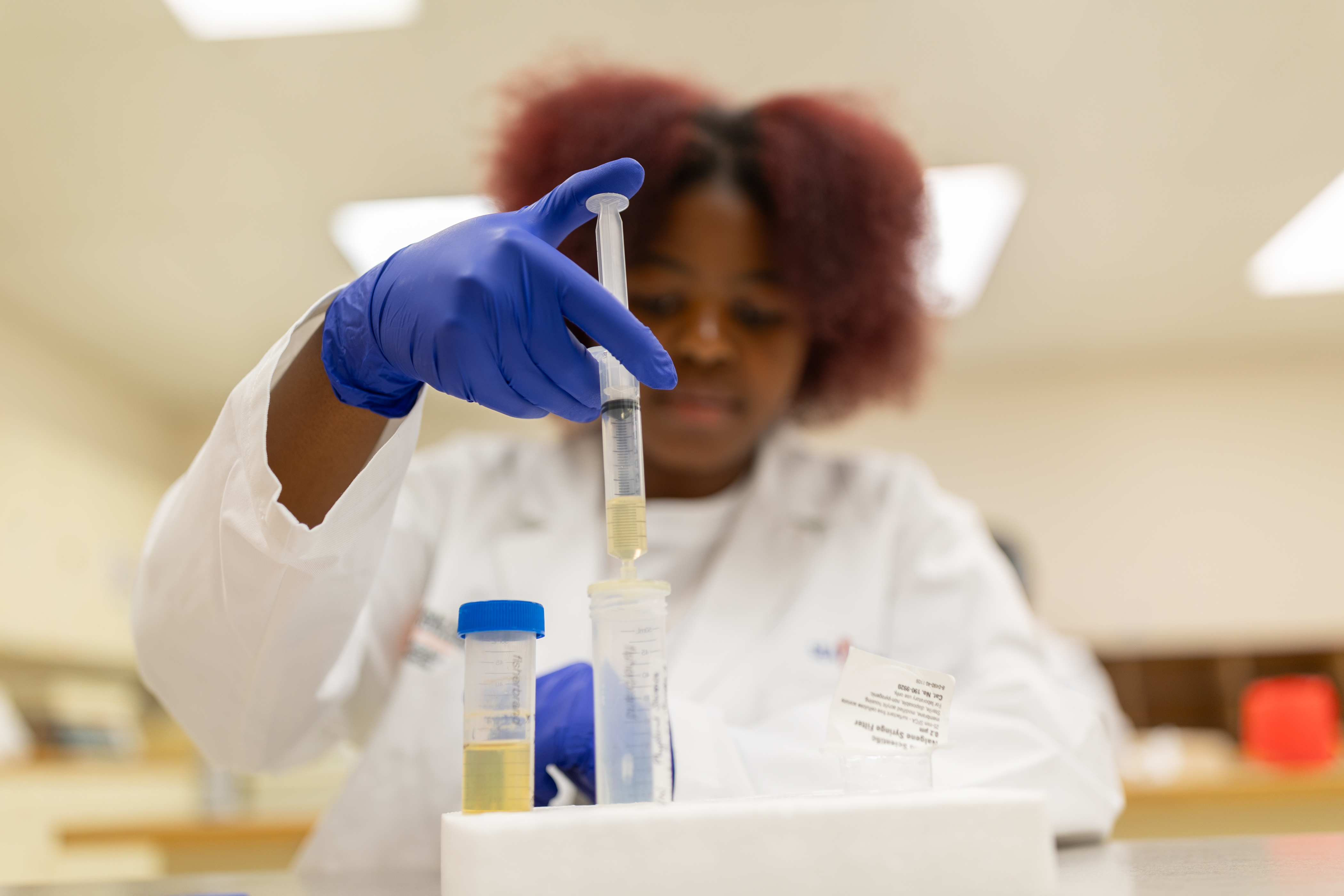 a researcher in PPE handling a syringe of liquid