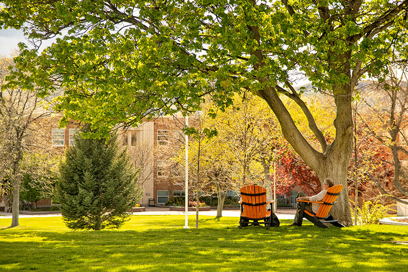 Two people sitting on Adirondack chairs at the Quad